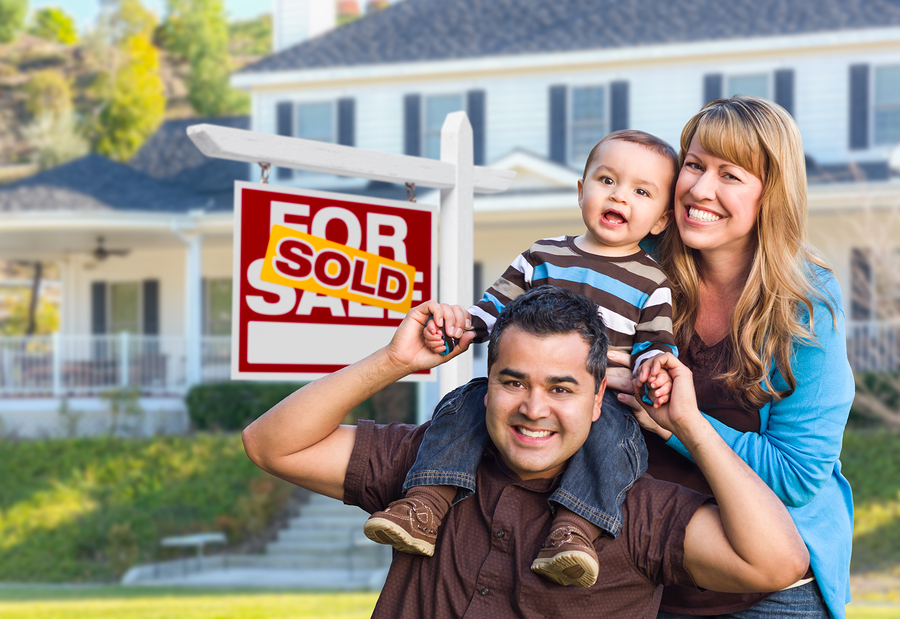 Happy Young Family in Front of Sold Home For Sale FSBO Real Estate Sign and House.