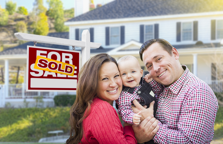Happy Young Family who bought a house for sale by owner In front of their new home with a "sold" sign