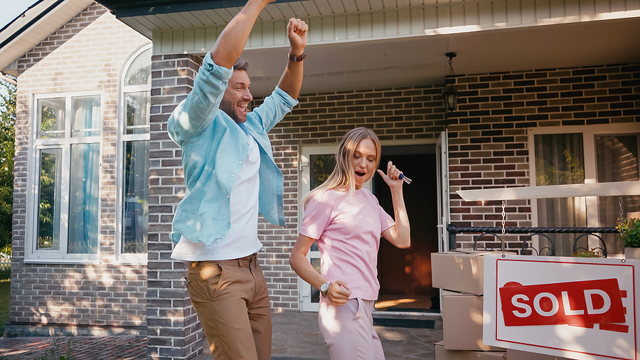 Happy home sellers dancing in front of "home sold" sign after selling their home